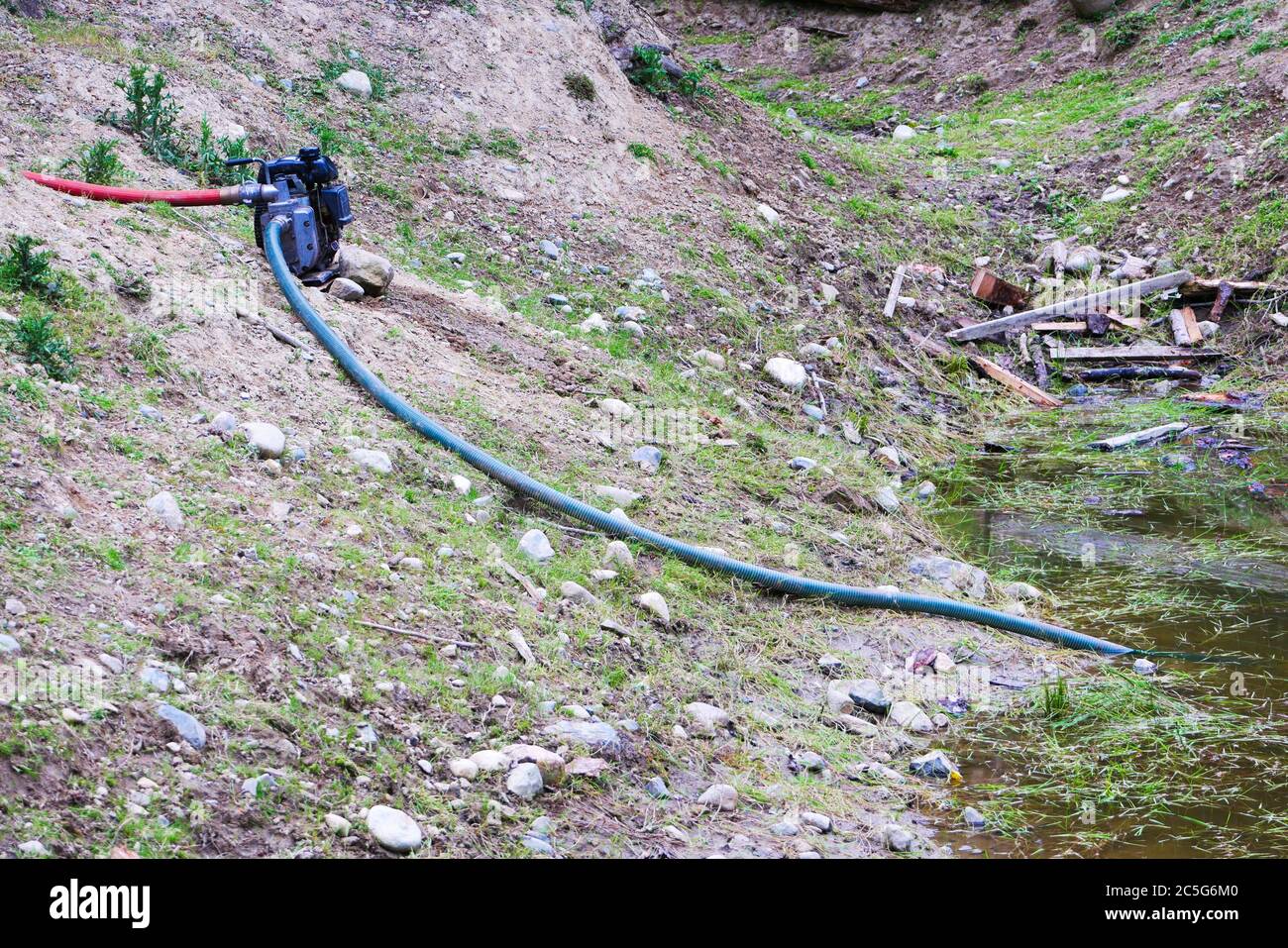 Pump drawing water from a pond with rocks and wood on the ground Stock Photo