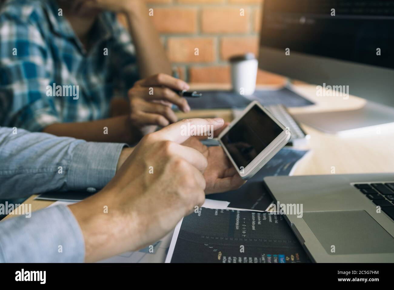 Software developers are using smart phones and analyzing together the code written in the program on the computer. Stock Photo