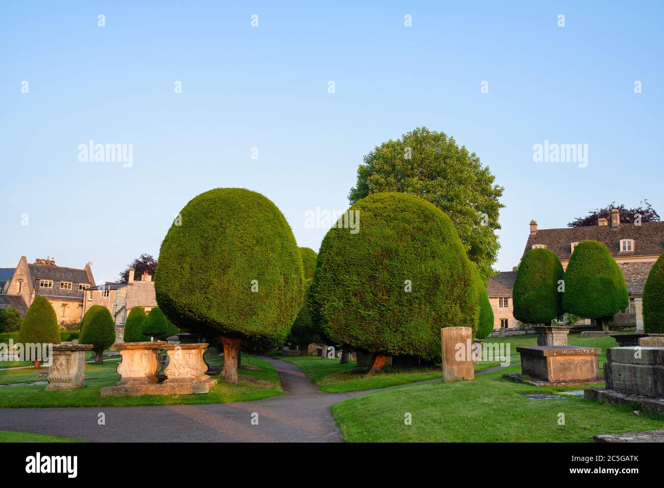Yew trees and headstones in St Marys churchyard at sunrise. Painswick, Cotswolds, Gloucestershire, England Stock Photo