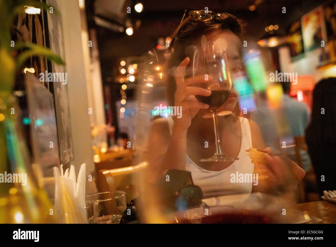 Young Vietnamese woman looking through her glass of wine in a bar, Ho Chi Minh City, Vietnam. Stock Photo
