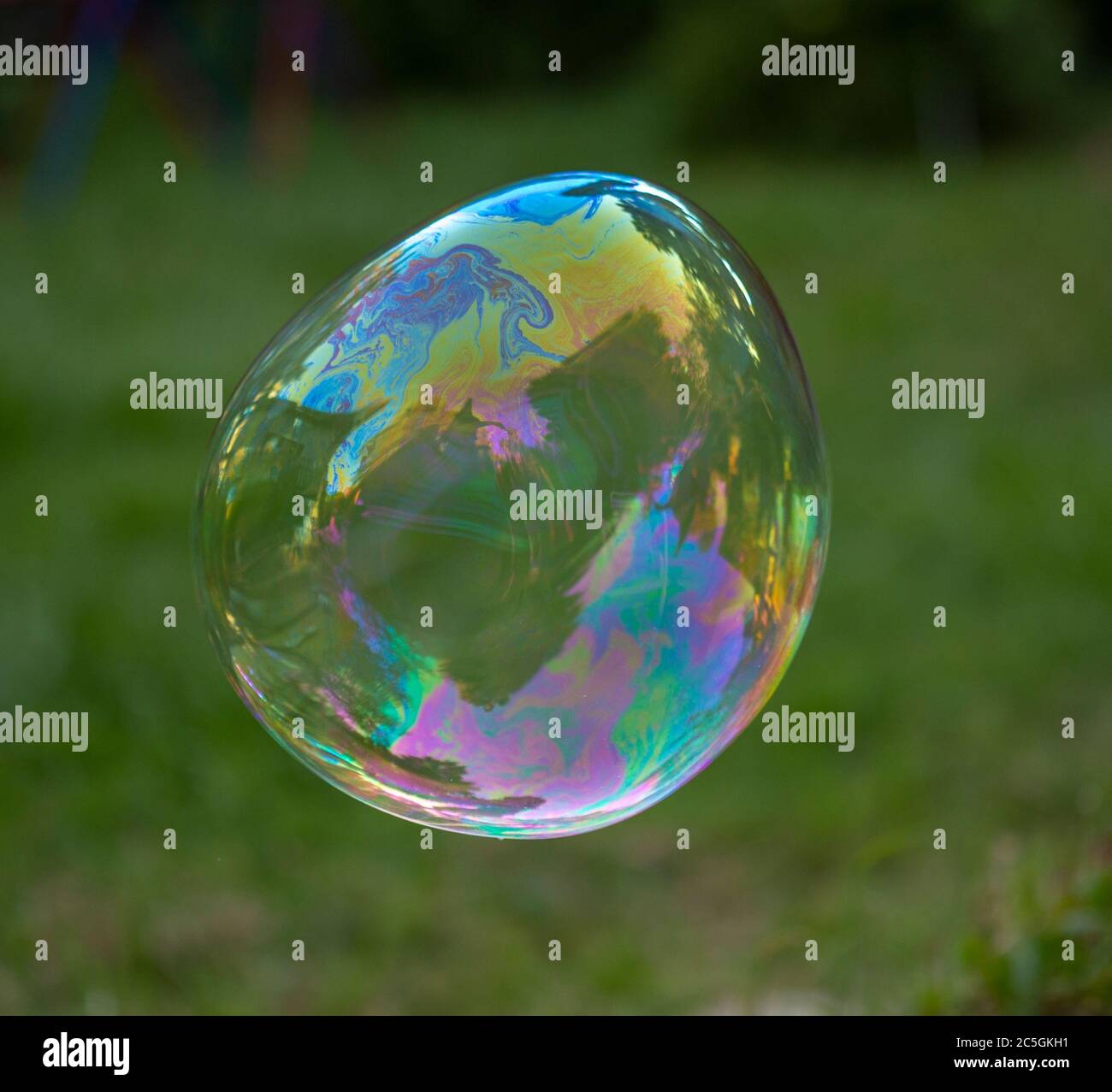 large soap bubble in focus floating in front of a blurred green garden ...