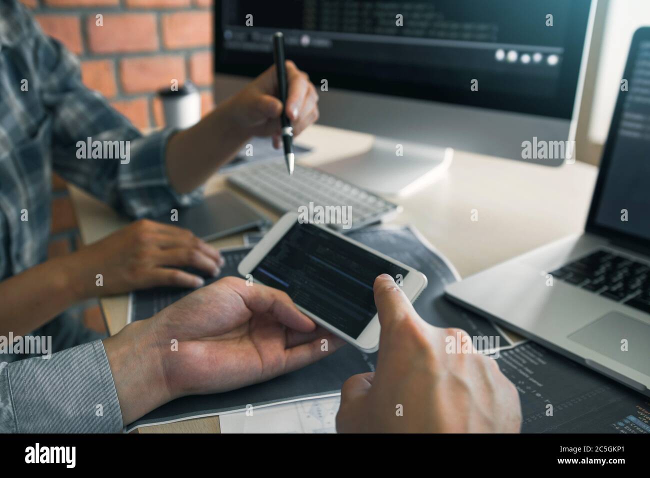 Software developers are using smart phones and analyzing together the code written in the program on the computer. Stock Photo