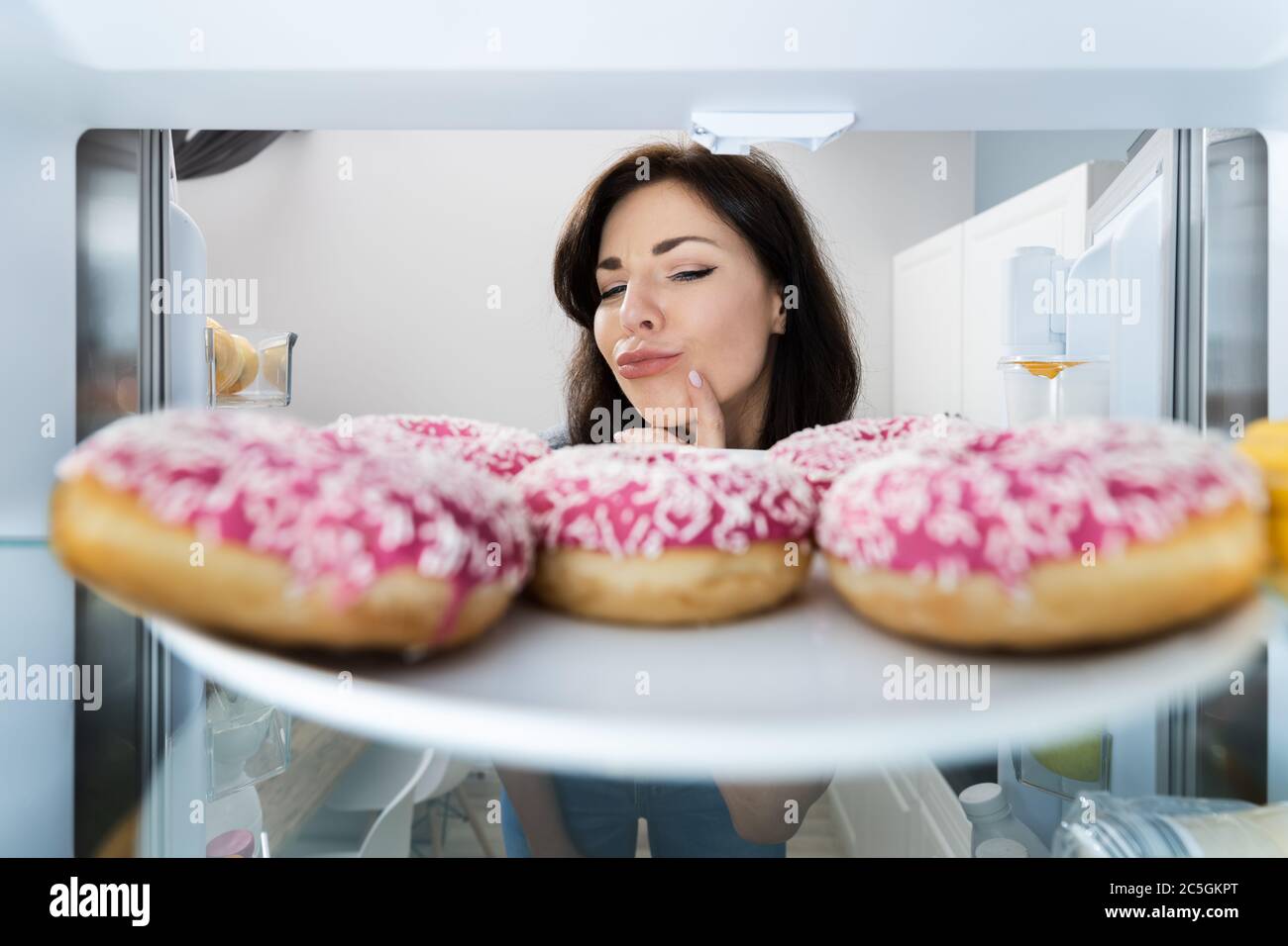 Confused Woman Thinking Looking At Sweets In Fridge Or Refrigerator Stock Photo