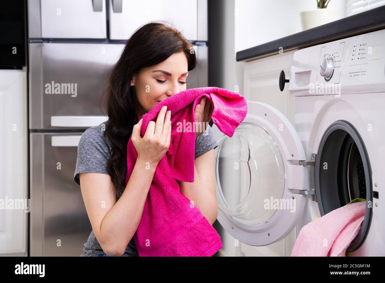 Woman Smelling Clothes At Home Doing Laundry Stock Photo