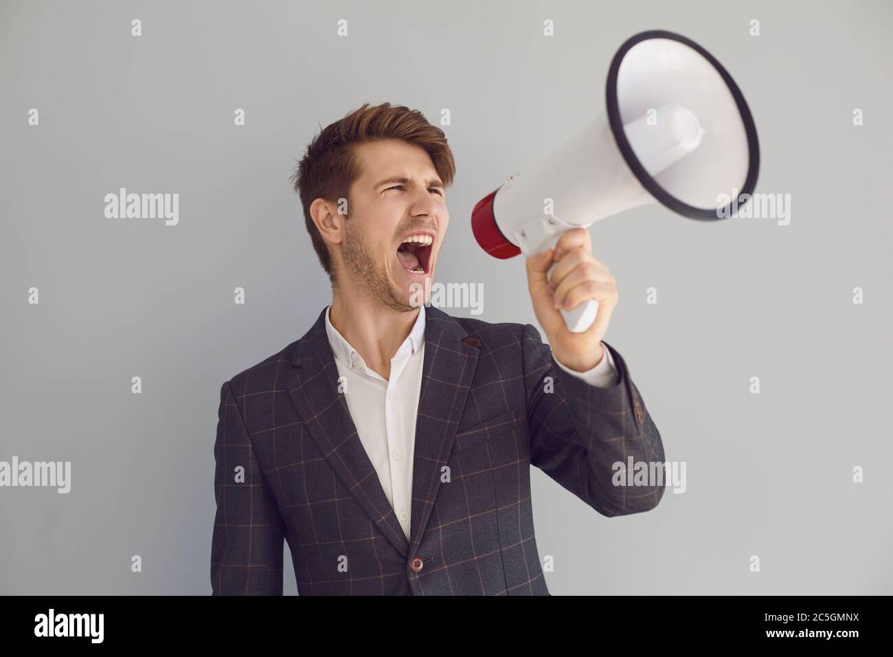 Stylish executive man screaming with loudspeaker on gray background Stock Photo
