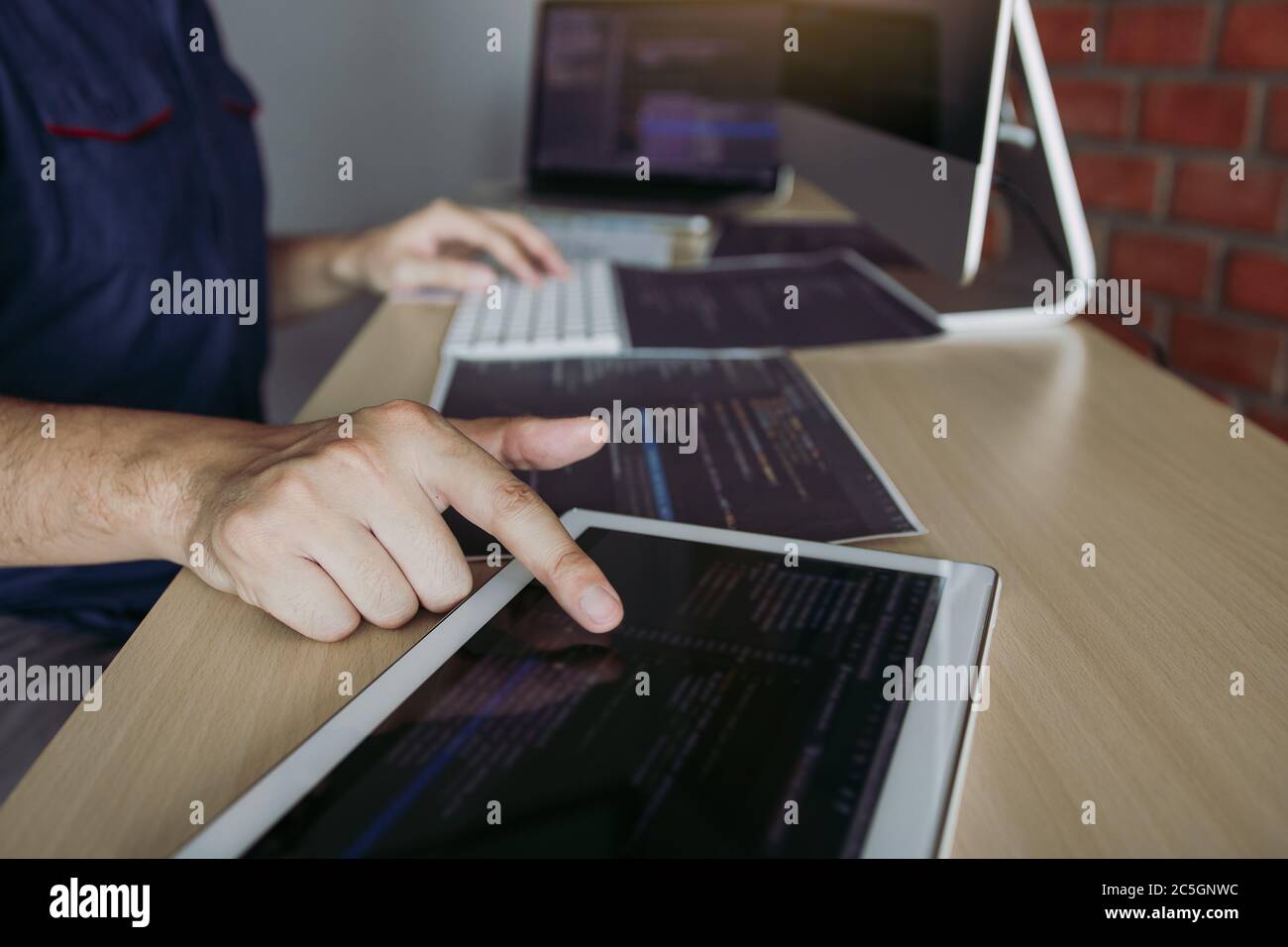 Software developer is pointing to the paper working and analyzing together the code written into the program on the computer. Stock Photo