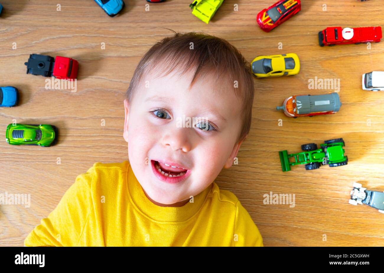 Cute little  kid boy playing with lots of toy cars indoor. Child wearing yellow shirt. Happy preschooler having fun at home or nursery. Big collection Stock Photo