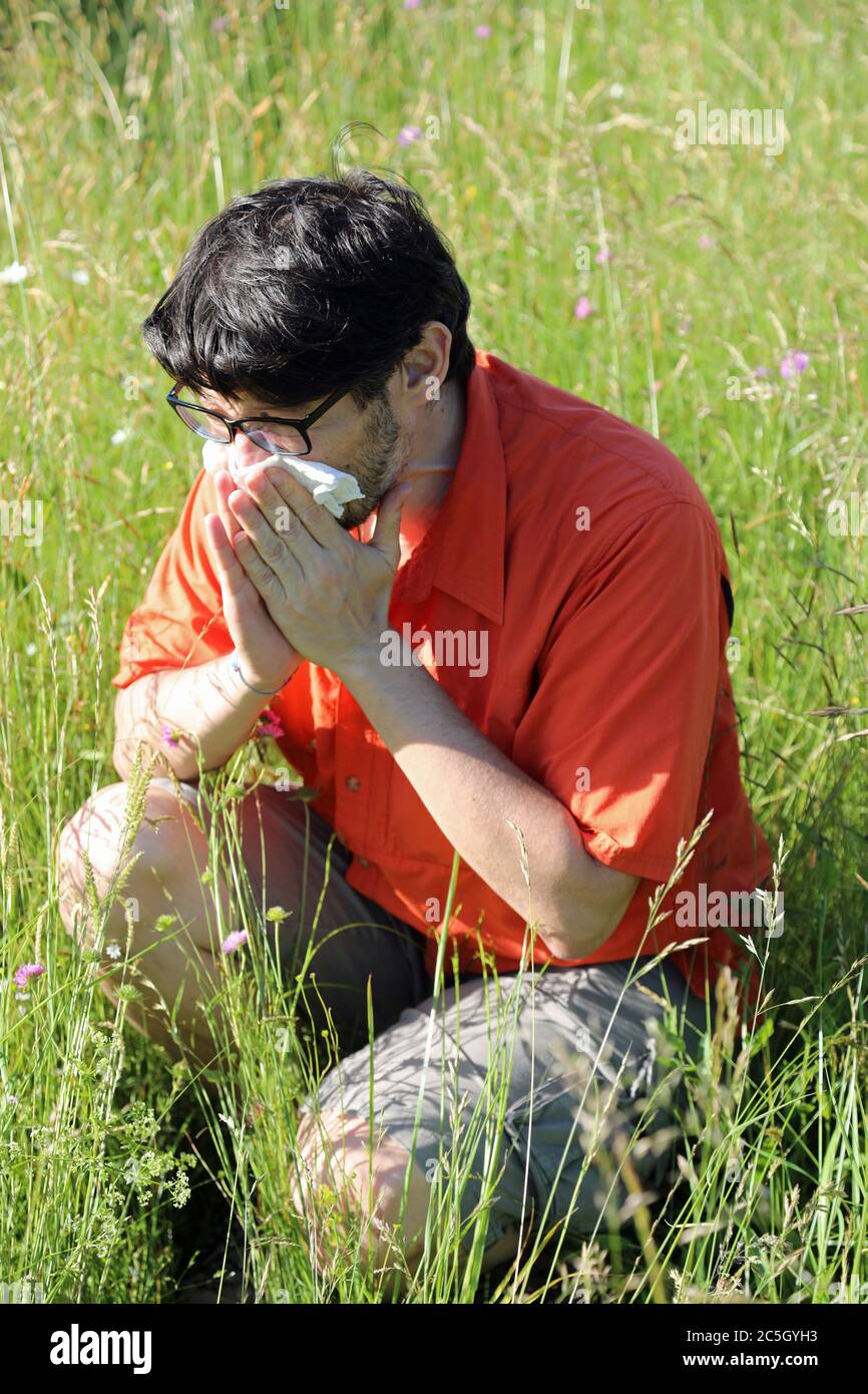 allergic boy blows his nose in the middle of the meadow in spring Stock Photo