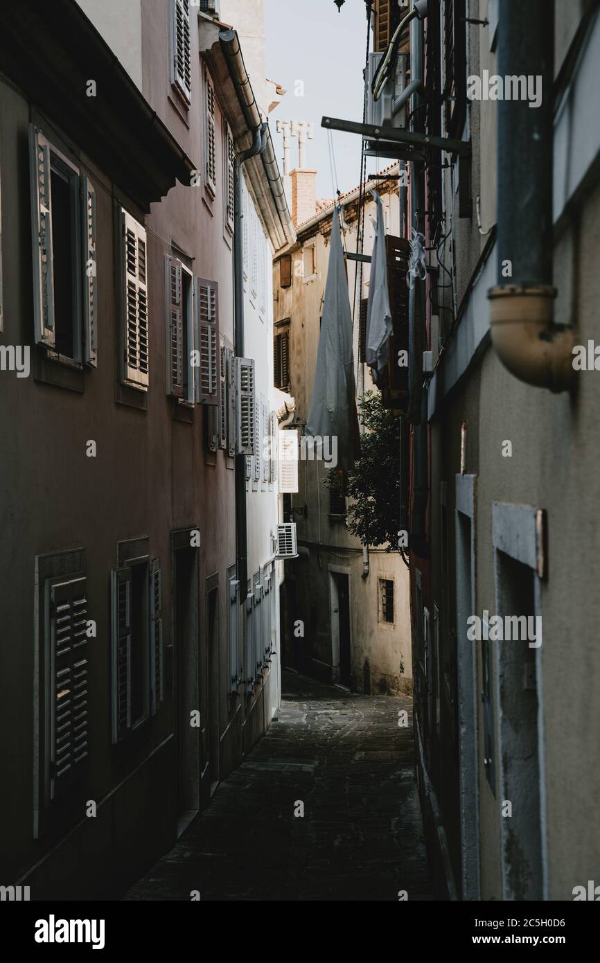 Romantic narrow alley of old historical coastal town Piran in Slovenia lined by houses with closed window shutters and hanging drying clothes Stock Photo
