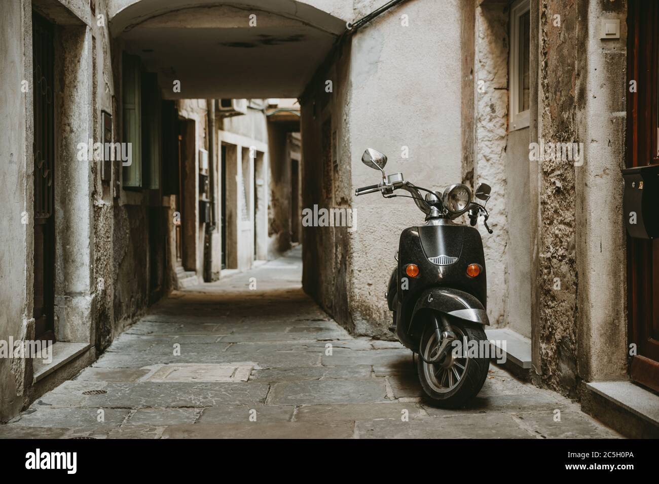 Lonely parked retro scooter in front of one house in old empty narrow alley with stone road of historic town of Piran in Slovenia Stock Photo