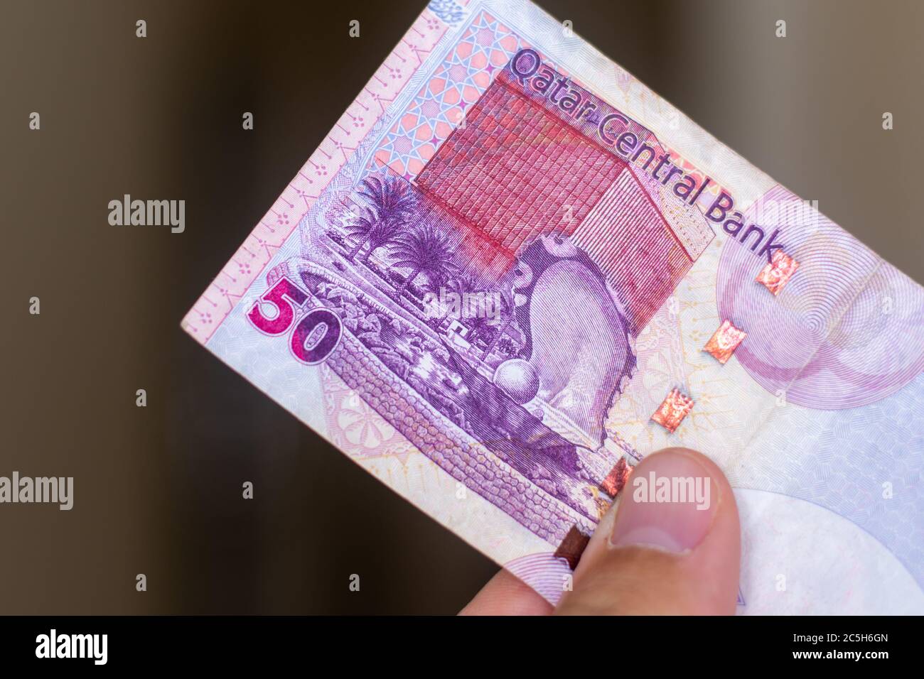 Persons hand giving the Currency of the Qatar - One fifty rial or riyal note spread out on a brown background. Money exchange. Stock Photo