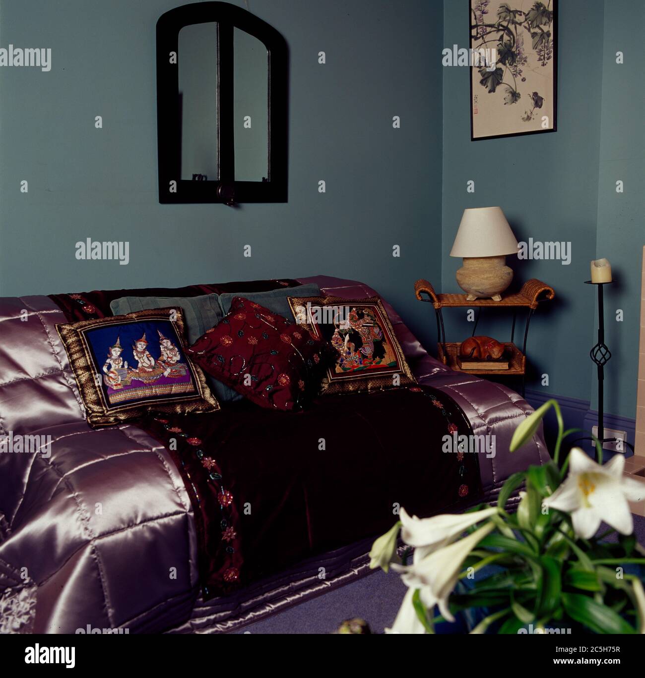 Satin throw, rug and cushions on divan in corner of room Stock Photo