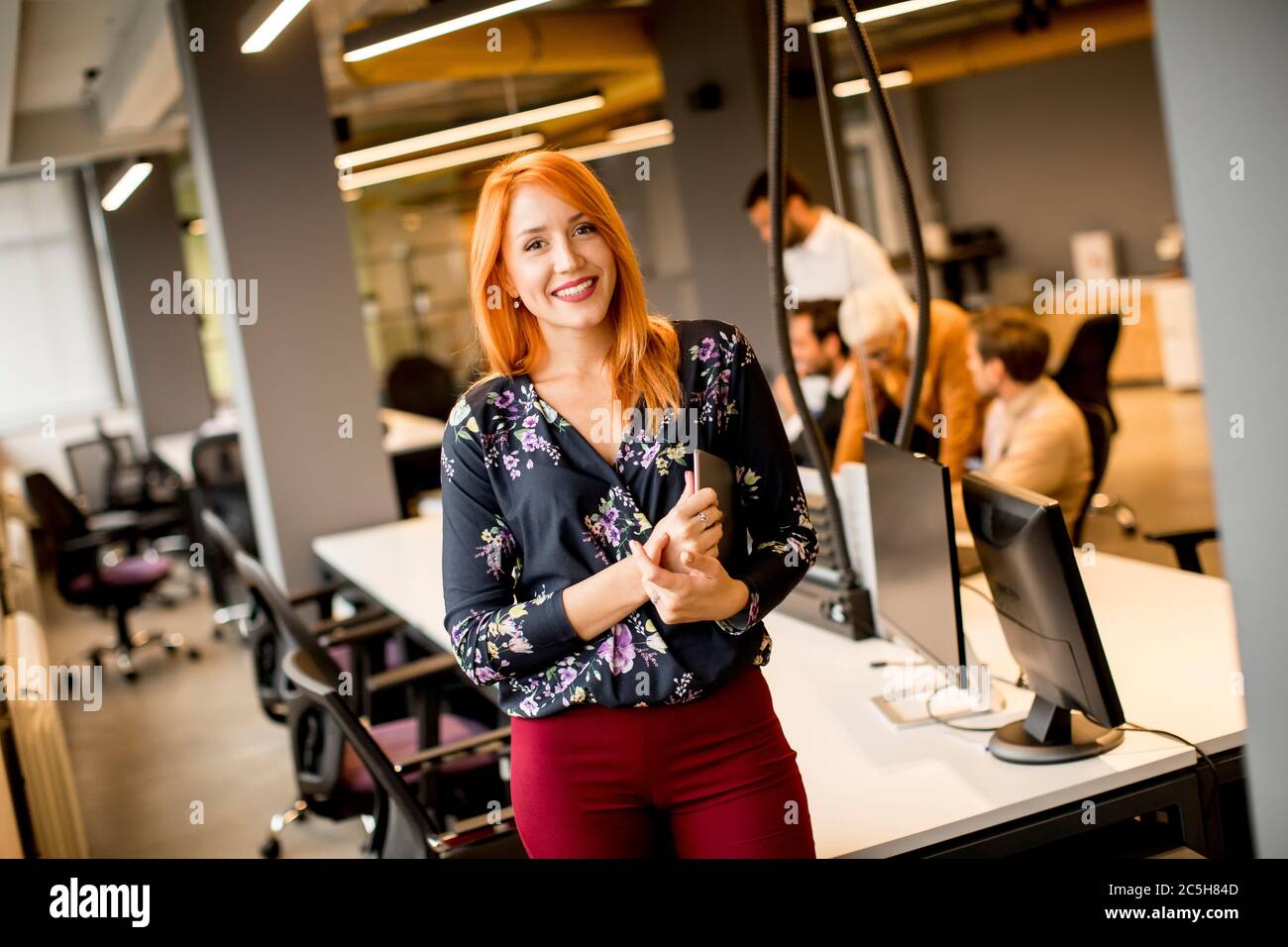 Pretty young businesswoman holding a digital tablet while in the background team working in the modern office Stock Photo