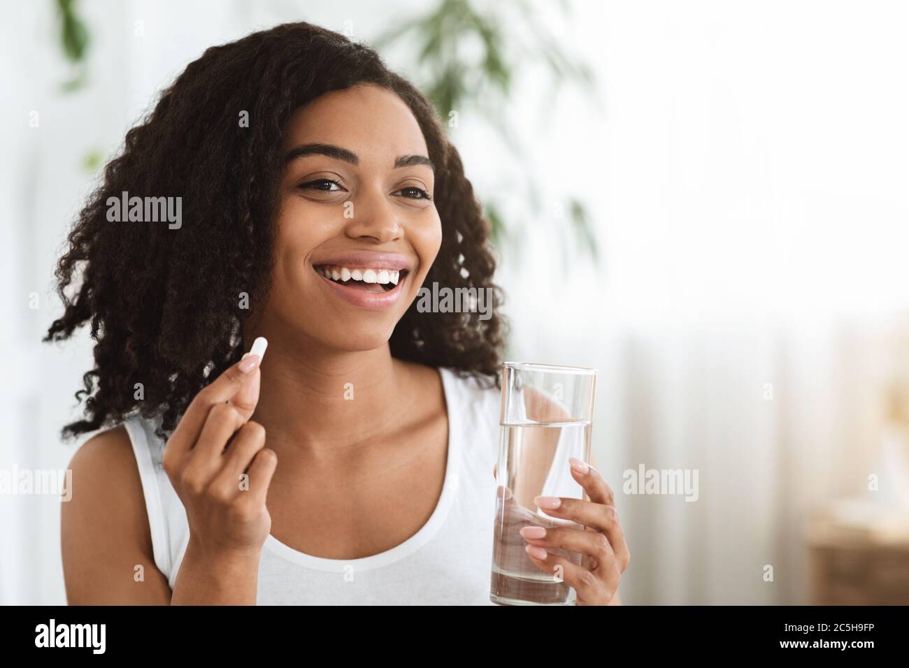 Healthy Diet Nutrition. Smiling Afro Woman Holding Vitamin Pill And Mineral Water Stock Photo