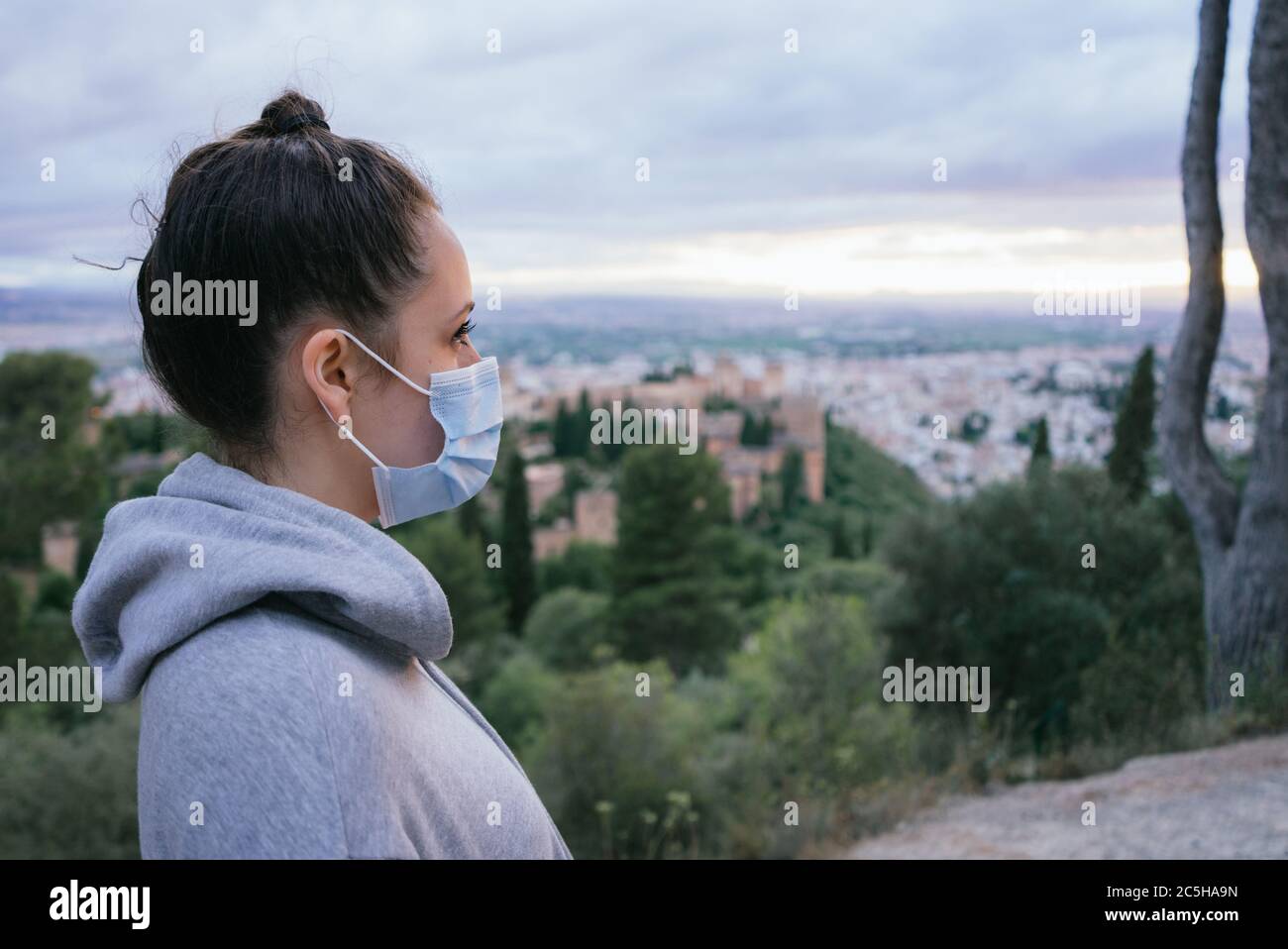 The close-up of a woman with a mask. Dangerous infectious disease. Young girl with mask in the city with the Alhambra in the background. Stock Photo