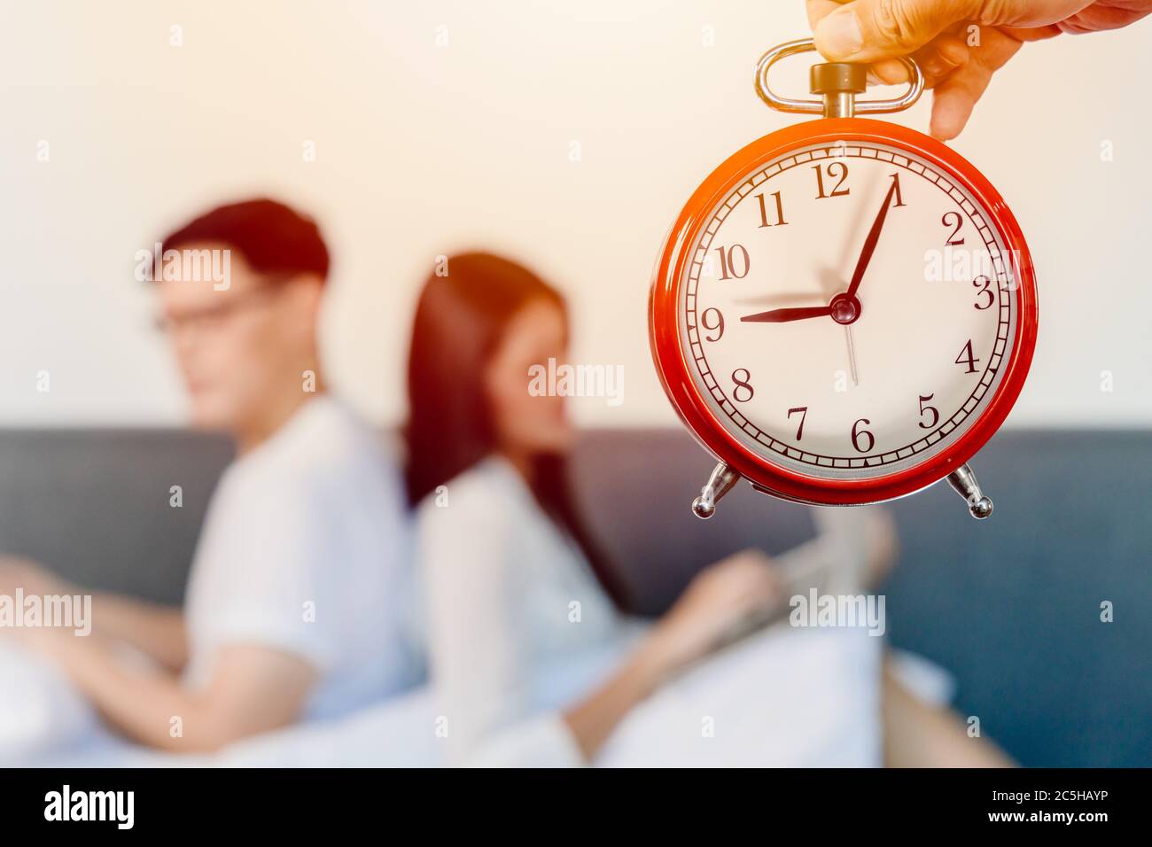 Alarm clock with blur people sitting facing back for bad relationship times of living together family hours or couple lover boring each other concept. Stock Photo