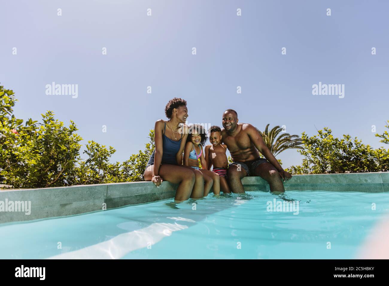 Beautiful young family sitting on the edge of swimming pool with their feet  in water. Young couple with their kids enjoying a hot summer day at the po  Stock Photo - Alamy