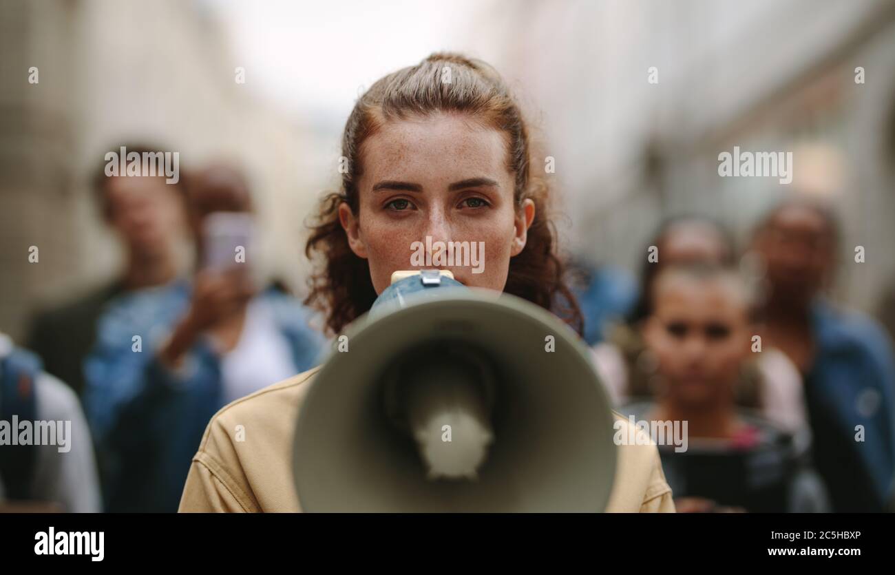 Female activist protesting with megaphone during a strike with group of demonstrator in background. Woman protesting in the city. Stock Photo