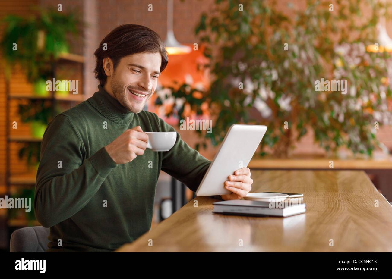 Happy young businessman reading news while drinking coffe at cafe Stock Photo
