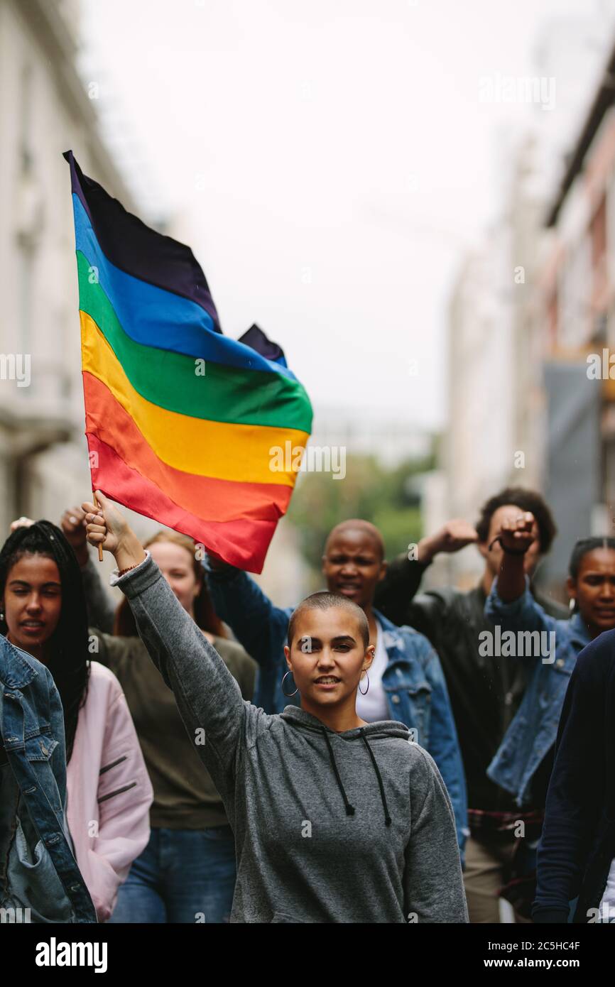 Female holding the gay rainbow flag at the Gay Pride Parade in city. Supporters and members of LGBTQI community during a Queer Pride Parade. Stock Photo