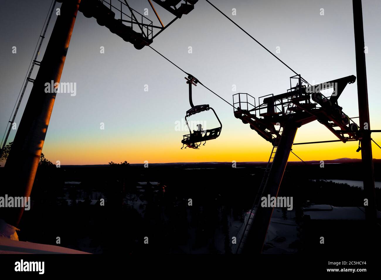 Silhouettes of skiers on chair lifts in the evening, sunset yellow light Stock Photo