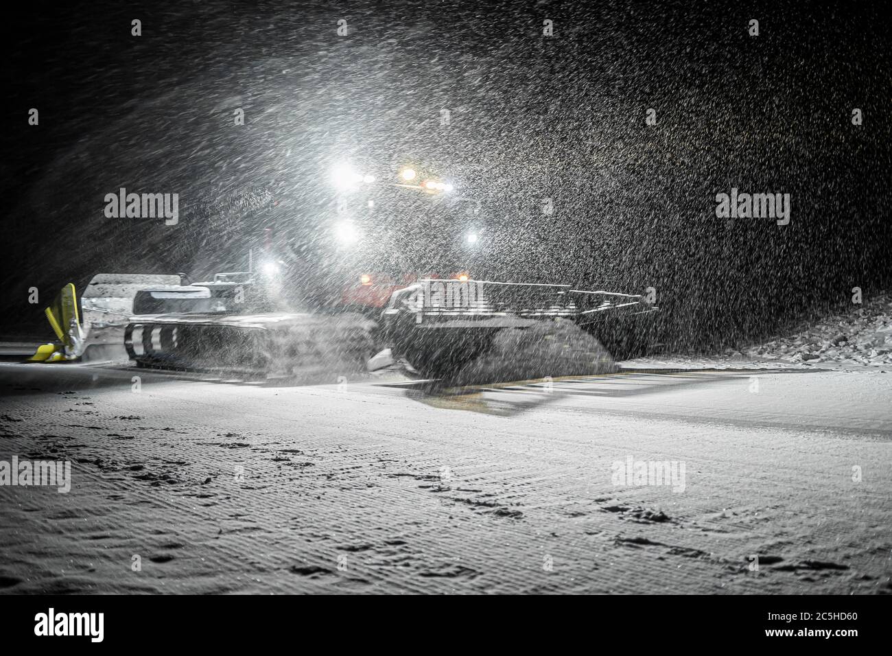 Snowcat with front lights preparing a slope at night in mountains at skiing resort with the snowfall Stock Photo