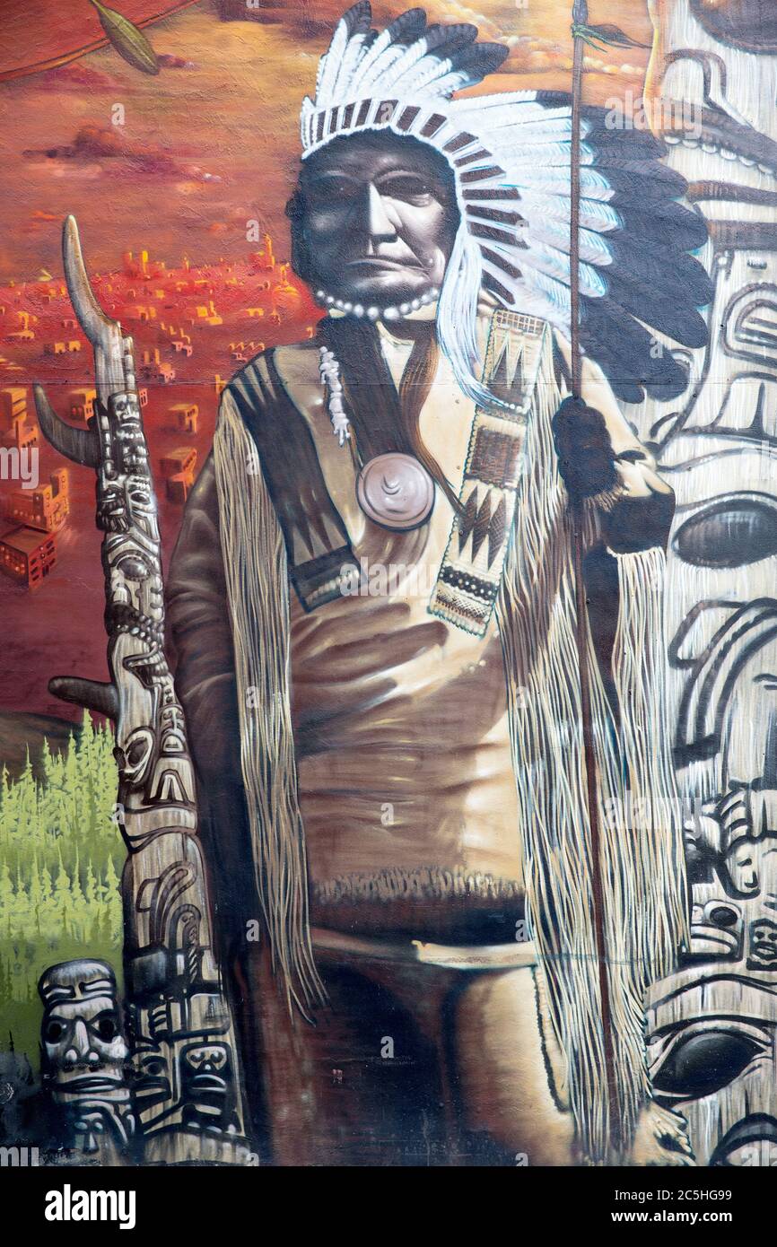 MONTREAL CANADA AUGUST 21 2014: Street art and graffiti. Exterior portrait of a Native American chief with spear, with totem poles in the background. Stock Photo