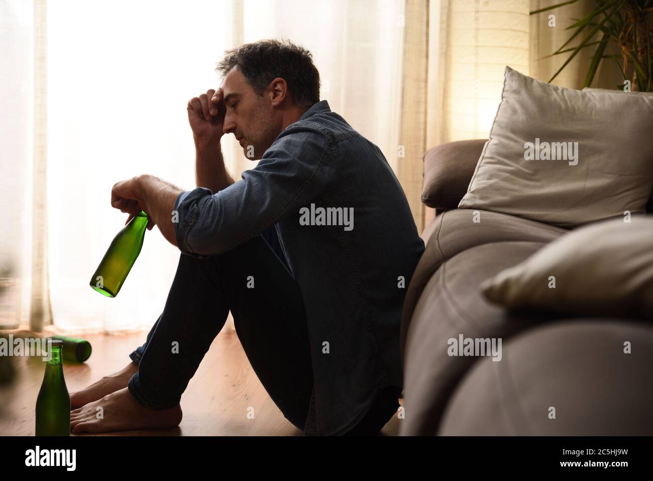 Sad and depressed man sitting in the living room drinking alcohol Stock Photo