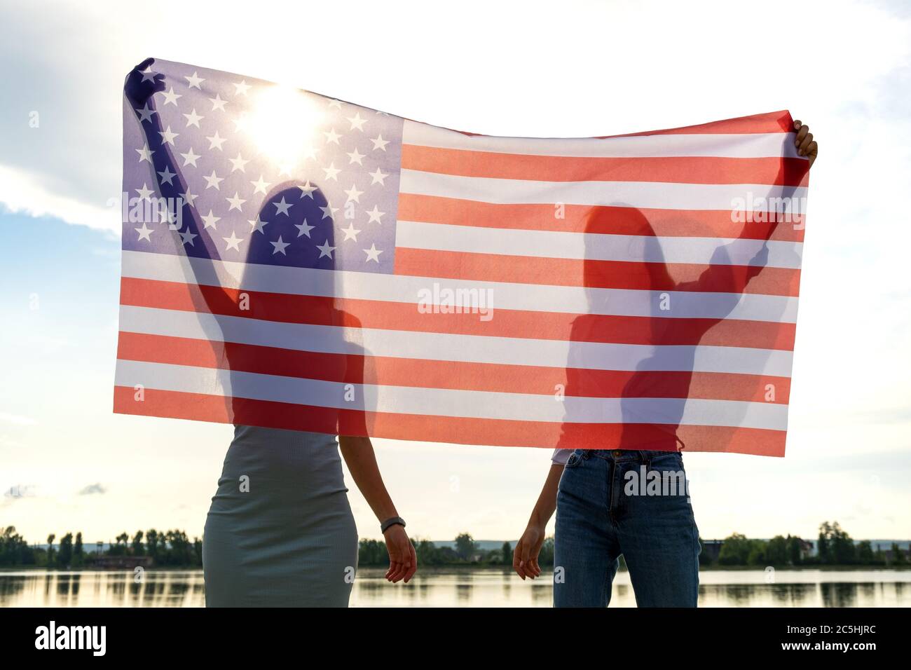 Silhouette of two young friends women holding USA national flag in ...
