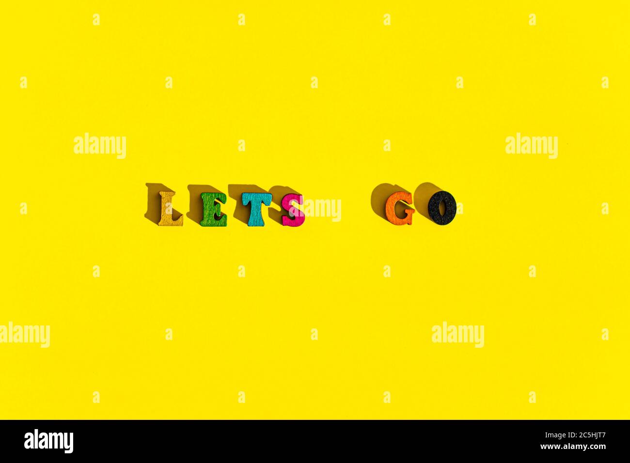 Flatlay of wood multicolored letters is inscription of lets go with shadows on bright plain yellow background. wishes and messages made up of models Stock Photo