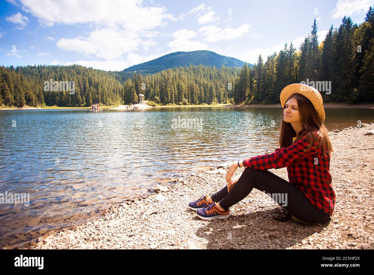 Tourist woman in hat sitting backwards and watching magic lake in mountains country landscape. Stock Photo