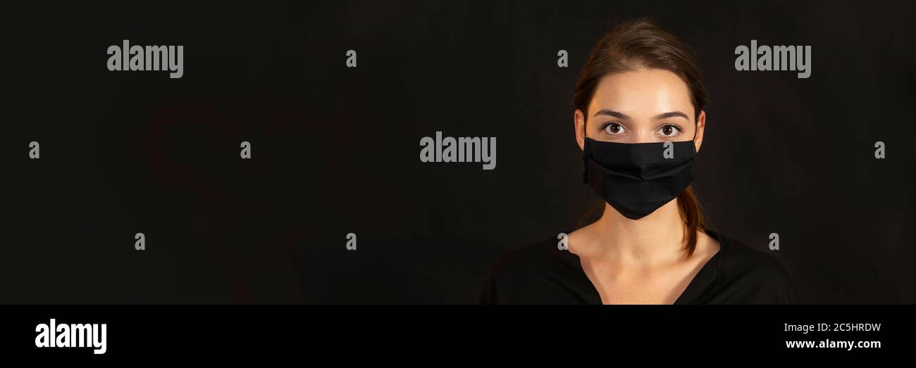 Banner with a young brunette girl in face mask on dark background. Stock Photo