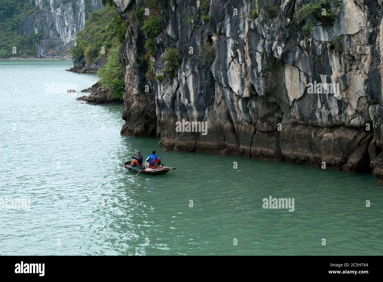 Ha Long Bay Vietnam, men fishing in small wooden boat near steep side of karst formation Stock Photo