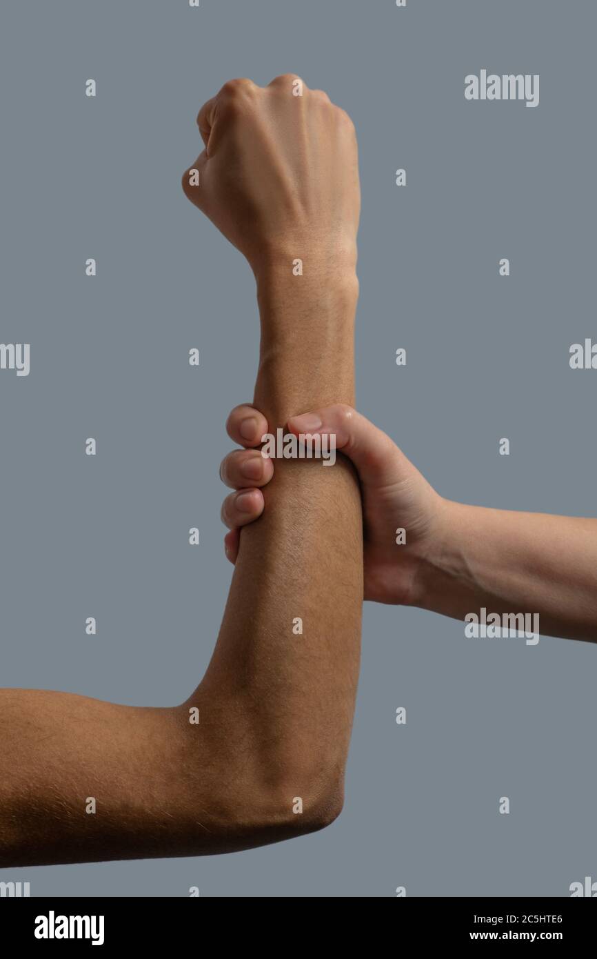 Close-up of light-skinned hand clenching dark-skinned forearm Stock Photo