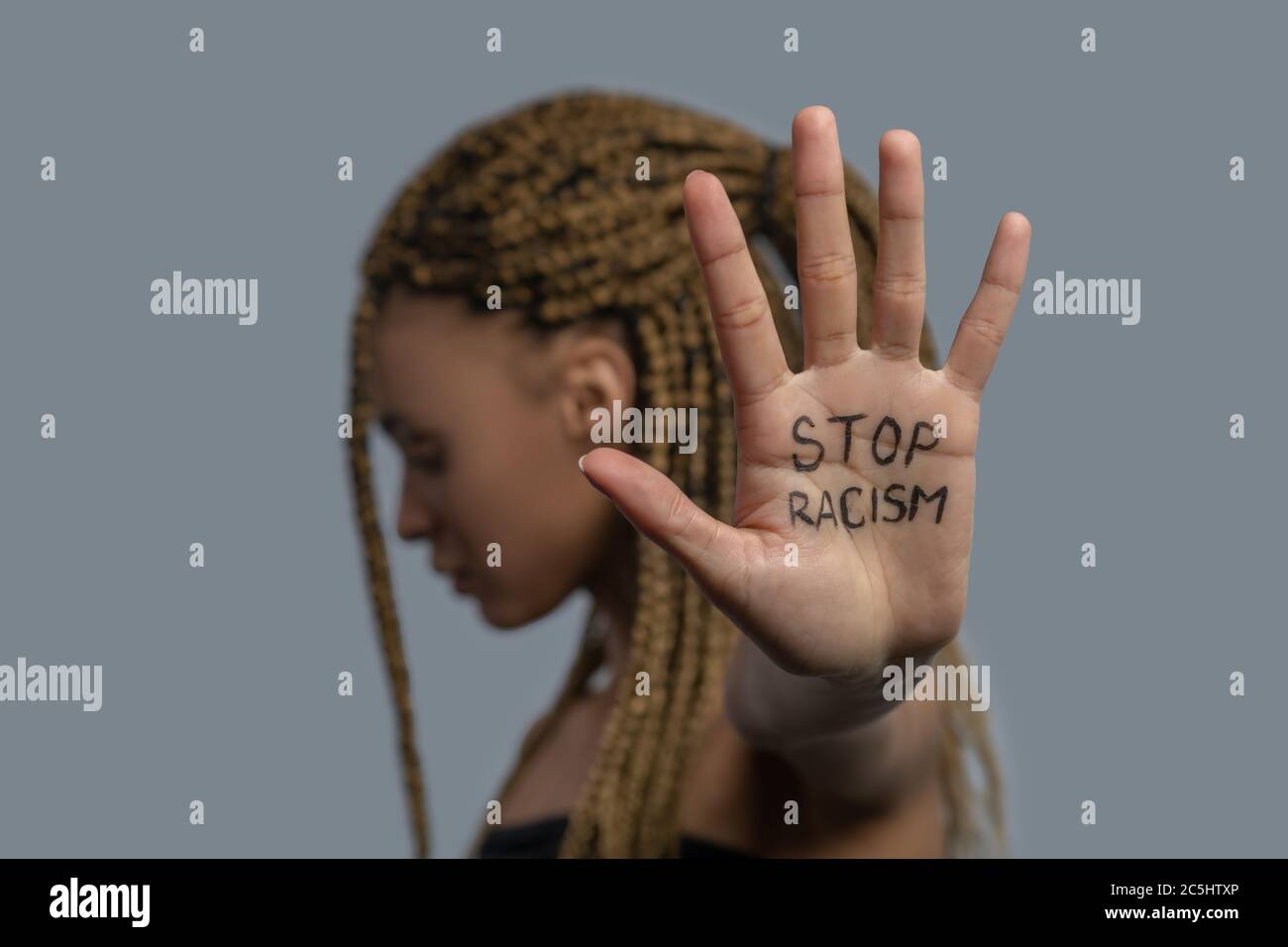 Young African American woman standing sideways, head down, showing palm with stop racism lettering Stock Photo
