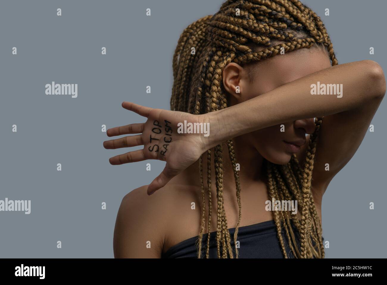 Young African American woman covering her face with elbow, showing palm with stop racism lettering Stock Photo