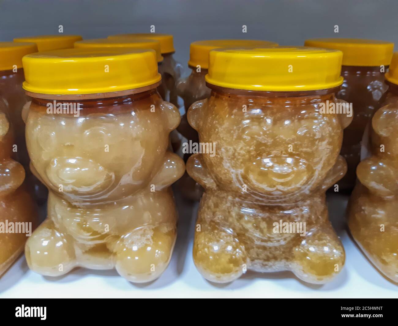 Many transparent plastic jars with yellow lids in the shape of a bear with different honey on shelf in shop. Stock Photo