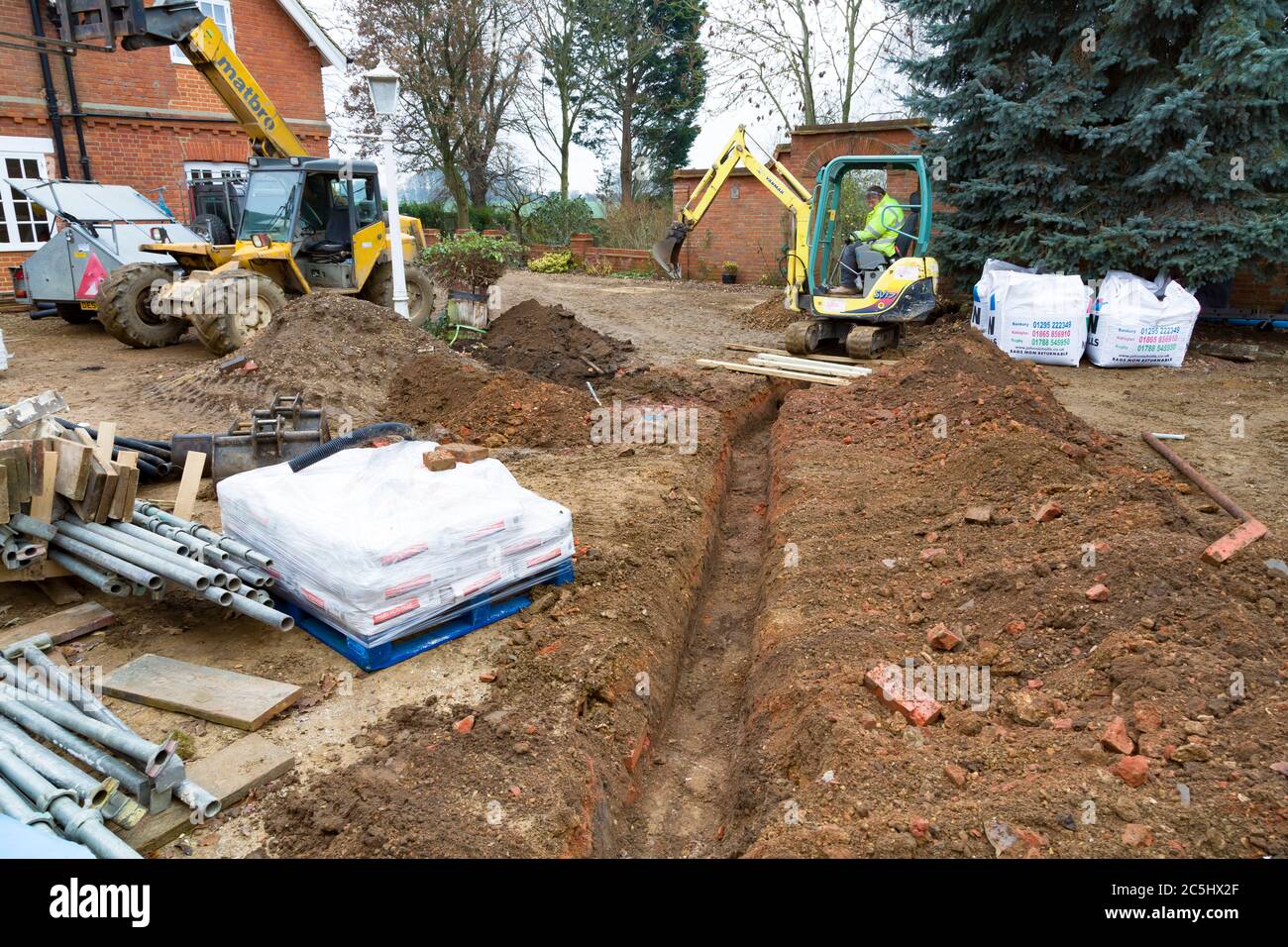 BUCKINGHAM, UK - December 02, 2016. Digger driver, digging a trench for drains on a UK building site Stock Photo