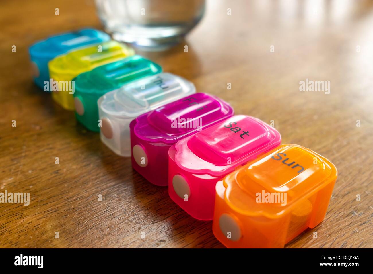 Shallow focus of a plastic pill dispenser seen on stable next to a glass of water. Stock Photo