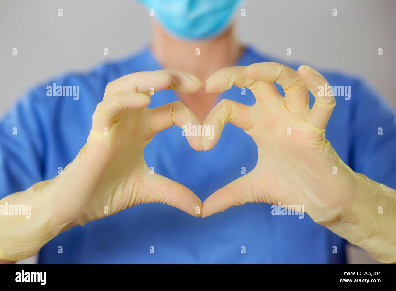 Hands in rubber gloves making the heart symbol in front of a healthcare professional in uniform. Stock Photo