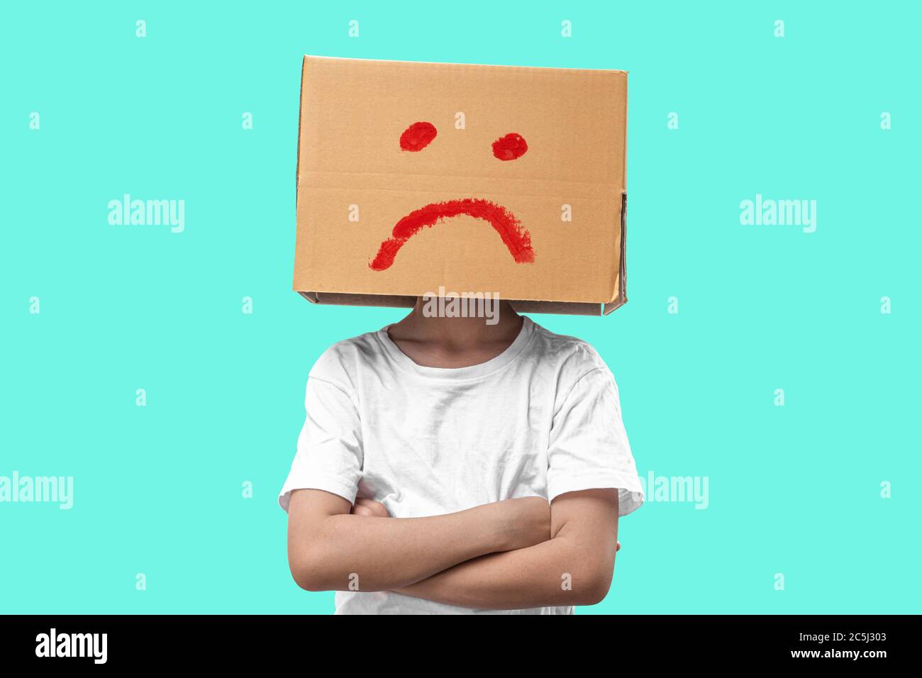Little girl wearing cardboard box on his head with unglücklich, Isolated on blue background. Stock Photo