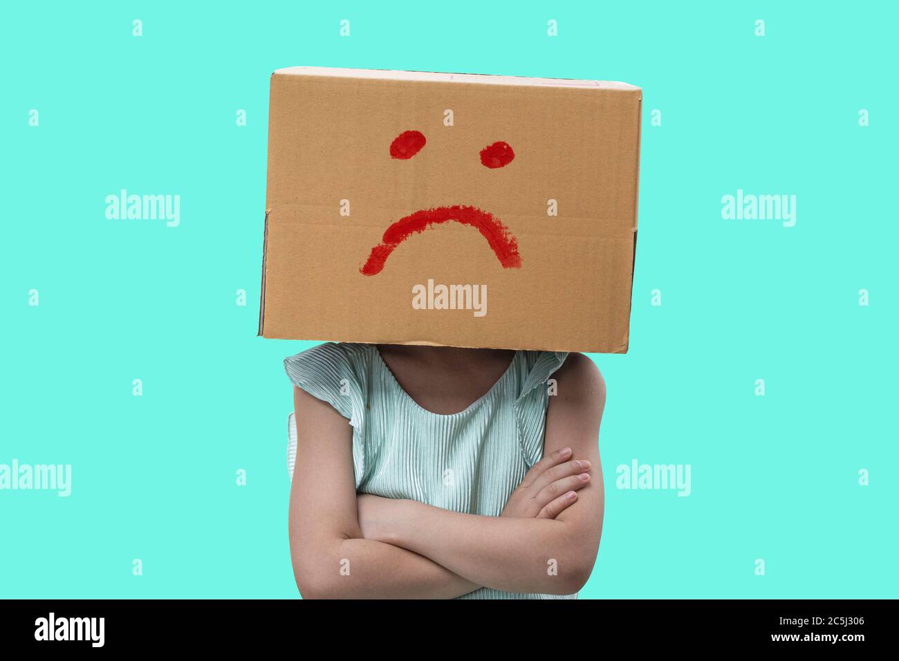 Little girl wearing cardboard box on his head with unglücklich, Isolated on blue background. Stock Photo