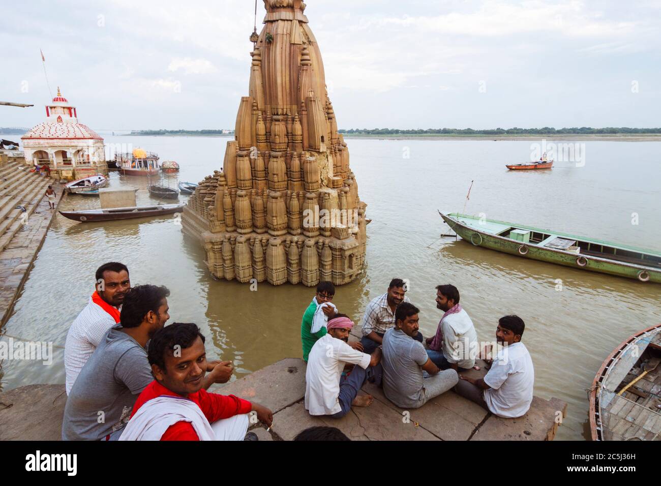 Varanasi, Uttar Pradesh, India : A group of men sit next to the partially sunken Ratneshwar Mahadev temple also known as the Leaning temple of Varanas Stock Photo