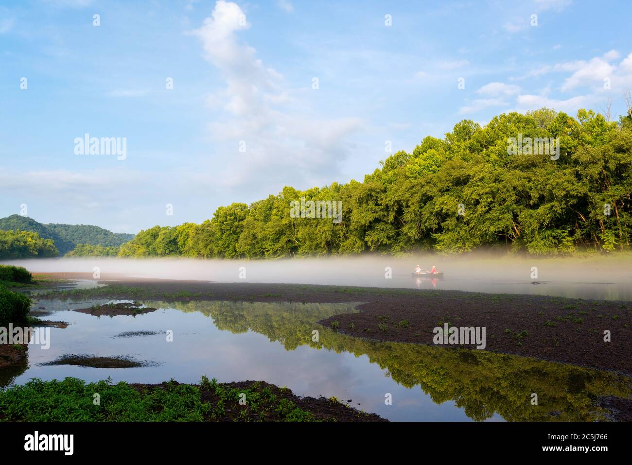 Couple in their small boat to row down the Little Tennessee River as dawn mist lifts at dawn near Gatlinburg, Tennessee, USA. Stock Photo