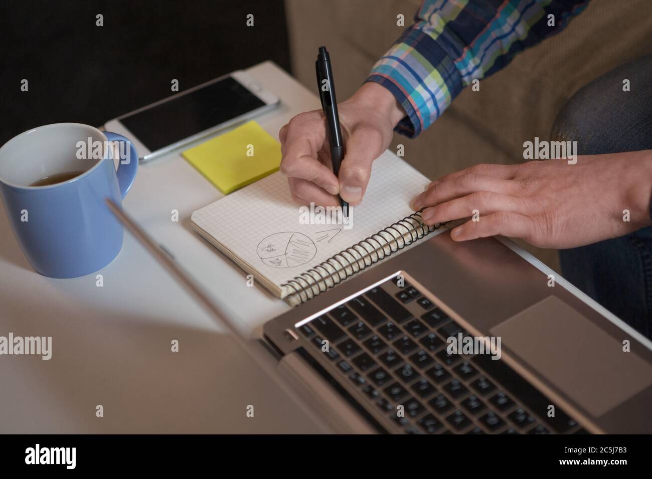 Freelancer man drawing diagram in notebook. Close up view. Working place of young hipster male working remotely at home Stock Photo