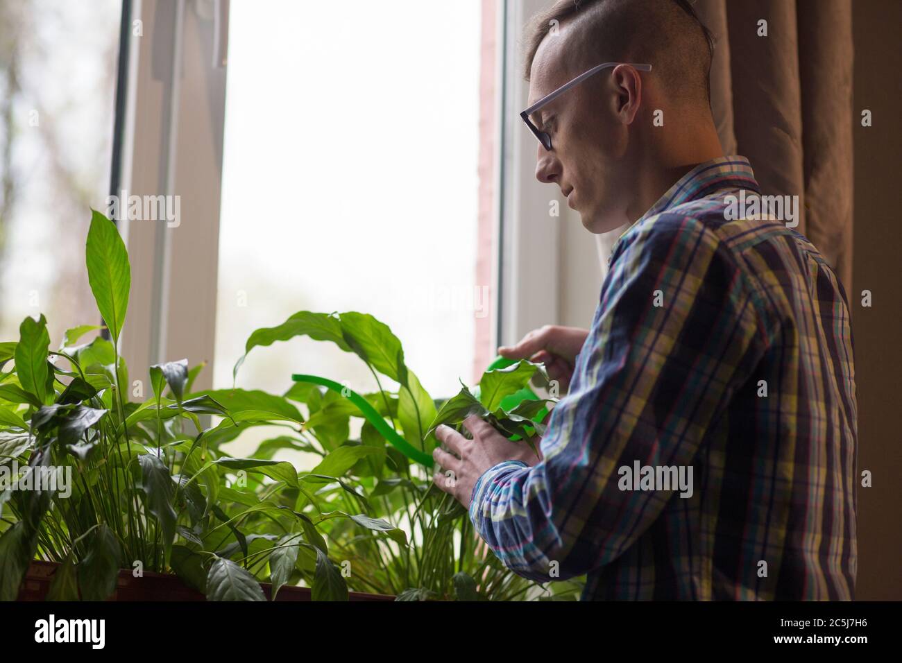 Young freelancer man watering flower pots during break in working process. Male taking care of palnts at home office Stock Photo