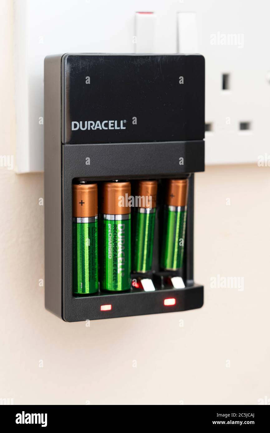 A Duracell rechargeable battery charger plugged into a plug socket with reusable AA and AAA batteries charging in a UK house Stock - Alamy