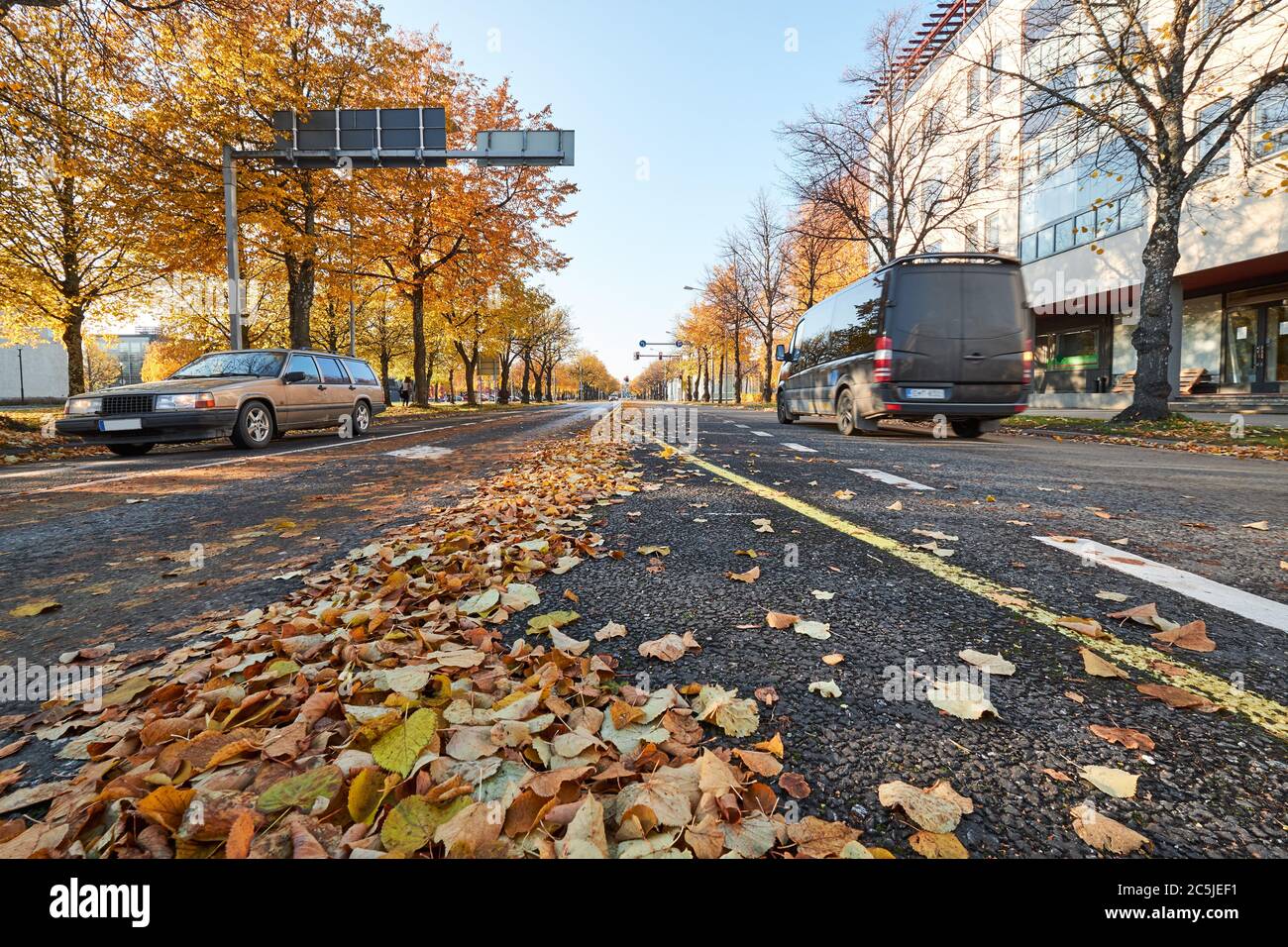 Street with moving car, autumn trees and leaves all around in the center of city. Finland Stock Photo