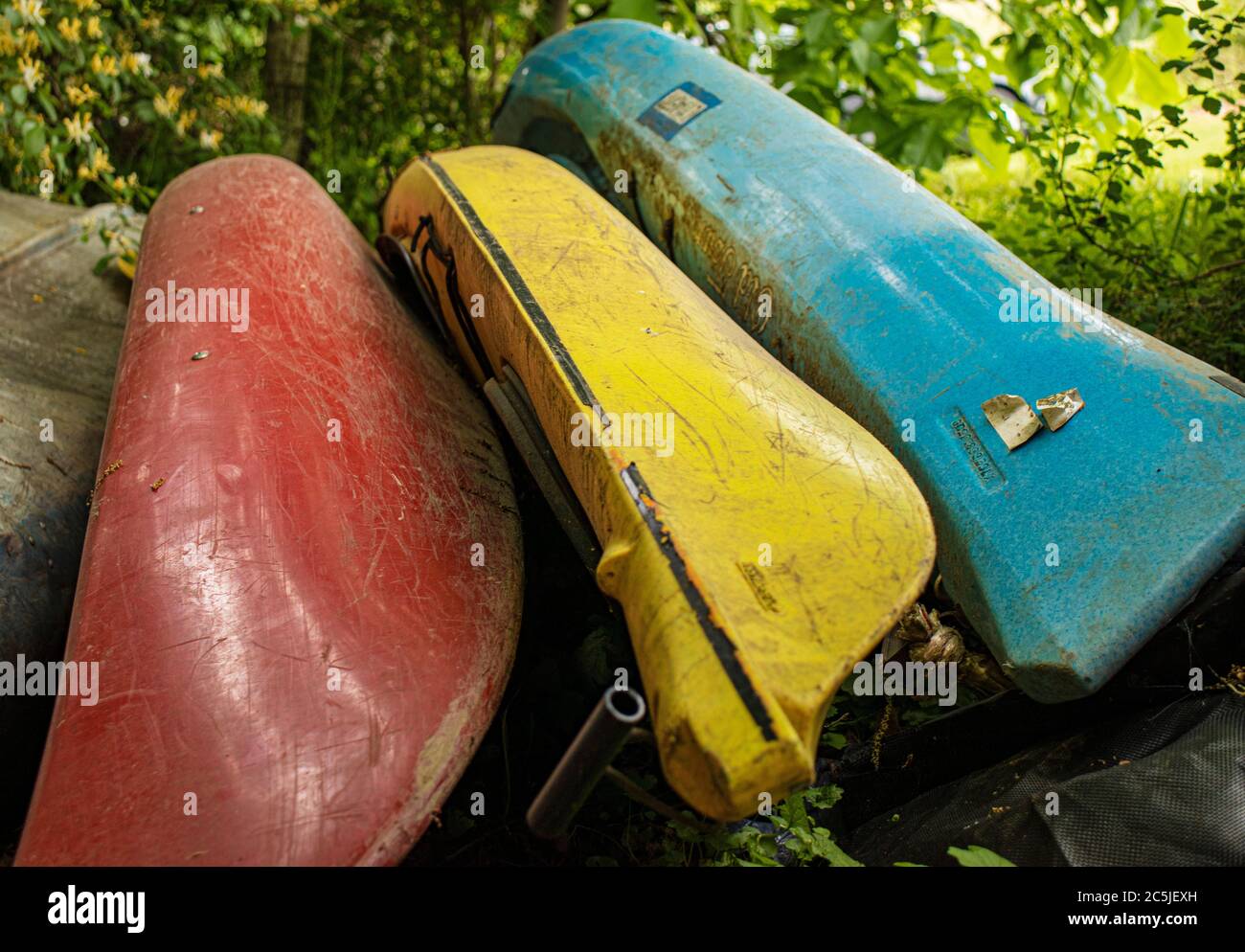 Three Kayaks in Primary Colors of Red Yellow and Blue Lying on Their Sides in Shrubbery Outside McClure in Central Pennsylvania Stock Photo