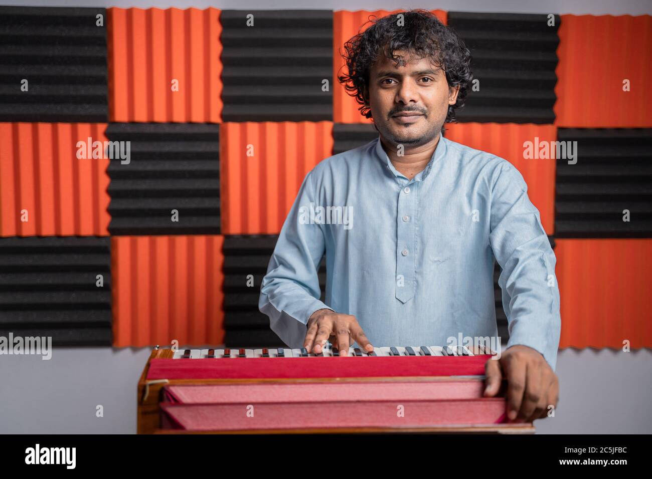 Young musician playing Indian music instrument Harmonium in studio. Stock Photo